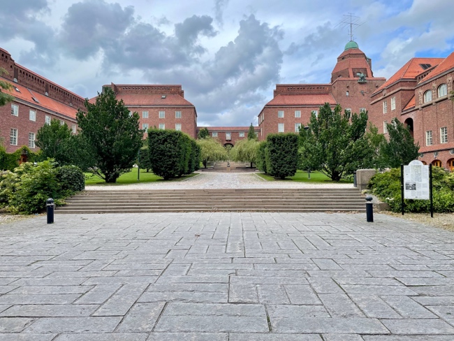 A brick building with trees and a walkway
Description automatically generated
